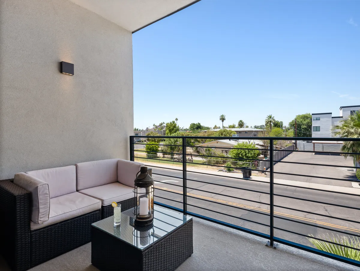 A private balcony with modern outdoor seating and a glass table, overlooking a lively street below. The setting is tranquil, with enough space for two to enjoy morning coffee or evening drinks together outdoors.