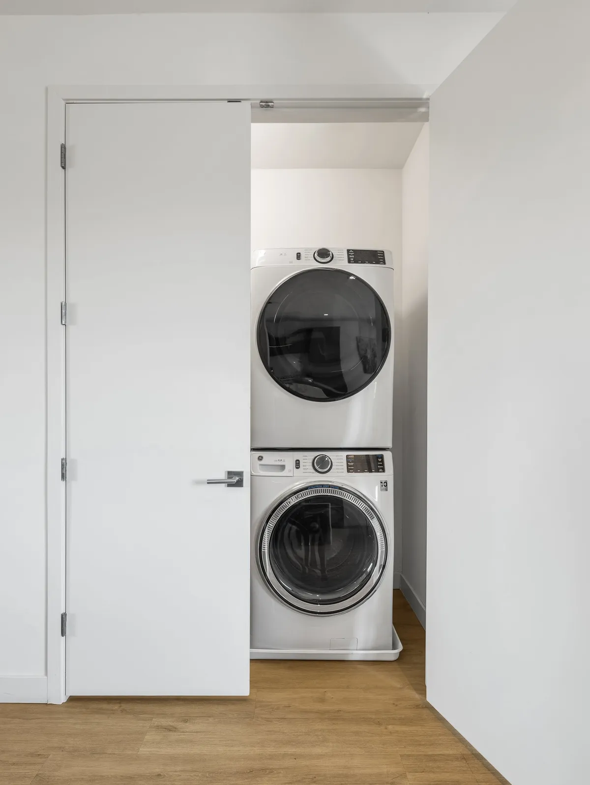 A dedicated laundry area featuring a washer and dryer, clean white walls, and a wood floor. The setup is practical, streamlined, and indicative of the professional standards of the building.