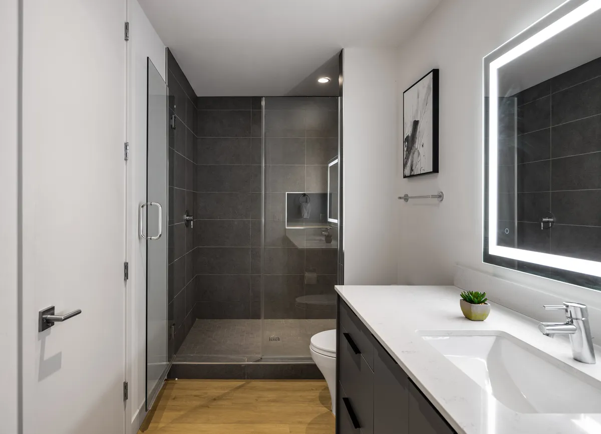A sleek, contemporary bathroom featuring a spacious shower area, a vanity with a sink, a backlit mirror, and tasteful framed artwork. The lighting and layout evoke a spa-like atmosphere, perfect for refreshing or unwinding after a long day.