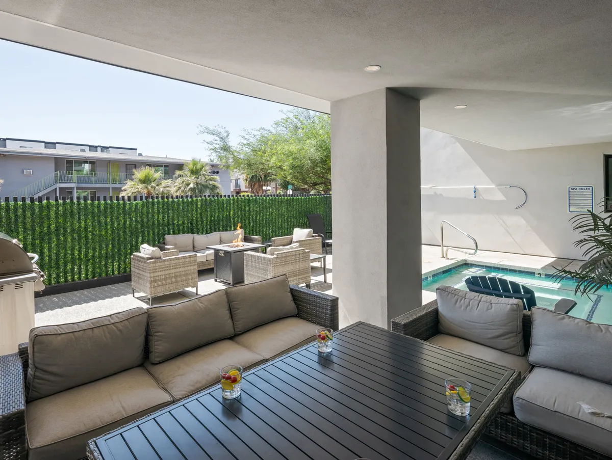 A sunny outdoor area featuring a sparkling swimming pool surrounded by lush greenery, with an inviting seating area where decorative drinks await. The scene is bright and intimate, perfect for relaxing or unwinding as a couple.
