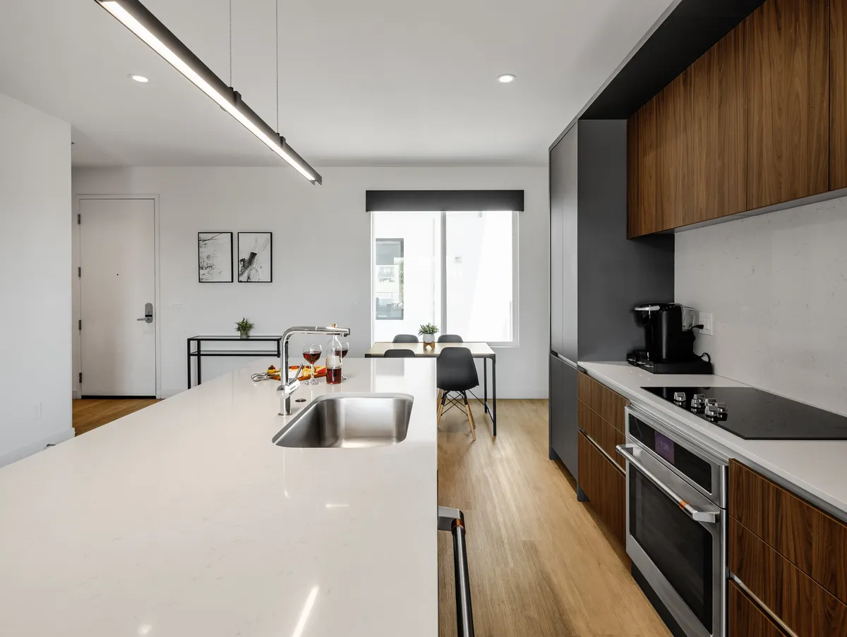 A contemporary kitchen space with a central island, dining area, and a window letting in natural light. The modern appliances and open layout encourage both solo and social activities, from cooking to entertaining.