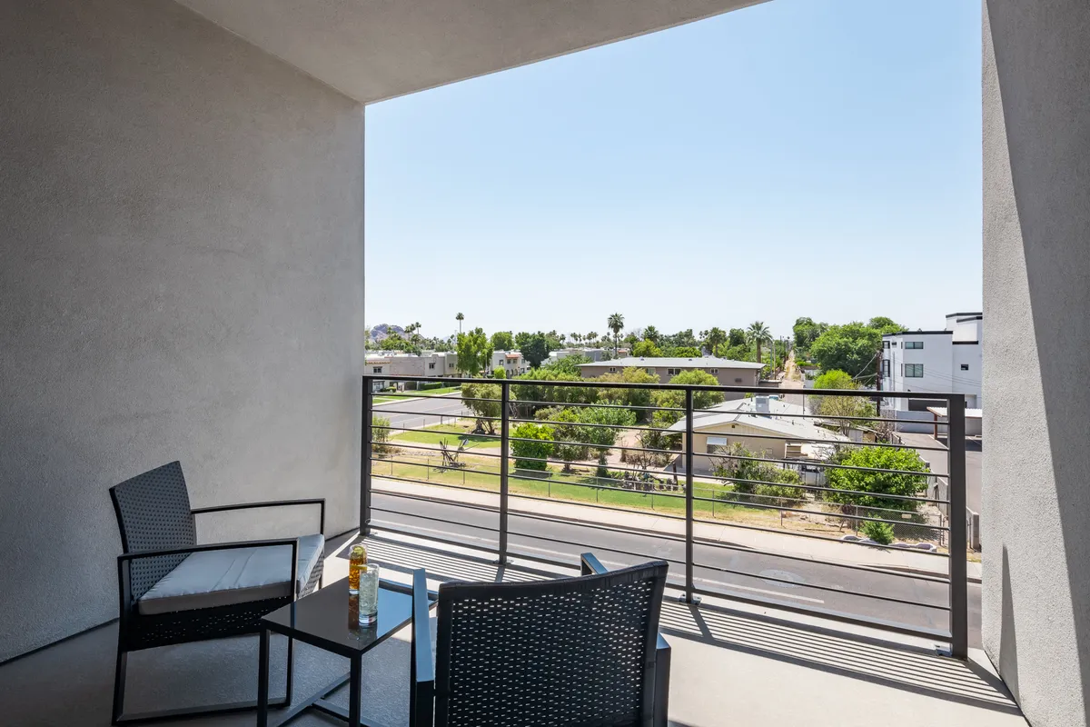 A private balcony with comfortable seating, a table set for drinks, and a tranquil view of the street and greenery. The mood is inviting, offering a serene spot for morning routines or sunset cocktails.