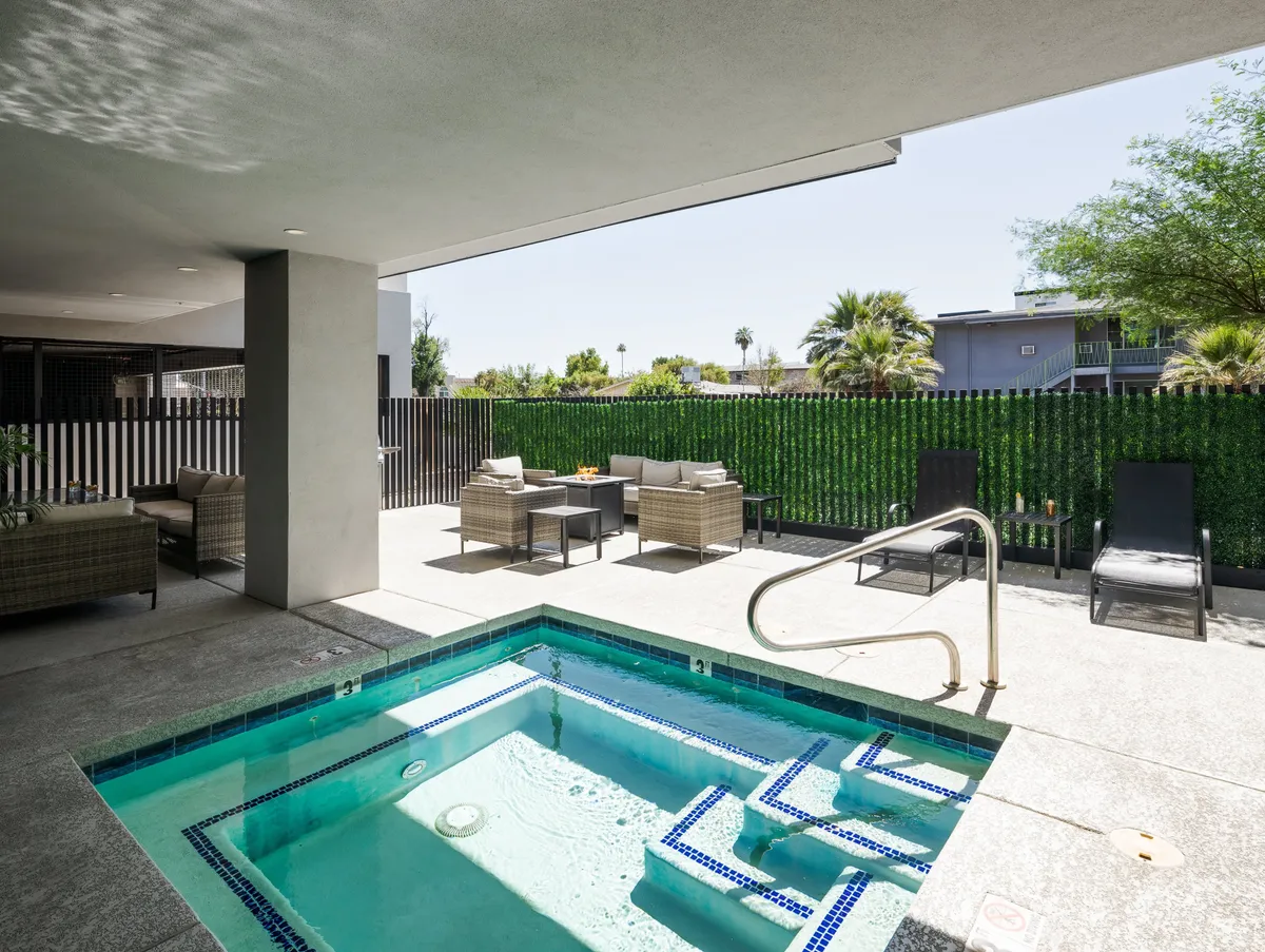 An exterior view of the hot tub and outdoor seating area, framed by lush landscaped greenery. The setting is tranquil and luxurious, perfect for relaxing by the pool or entertaining guests during sunset.