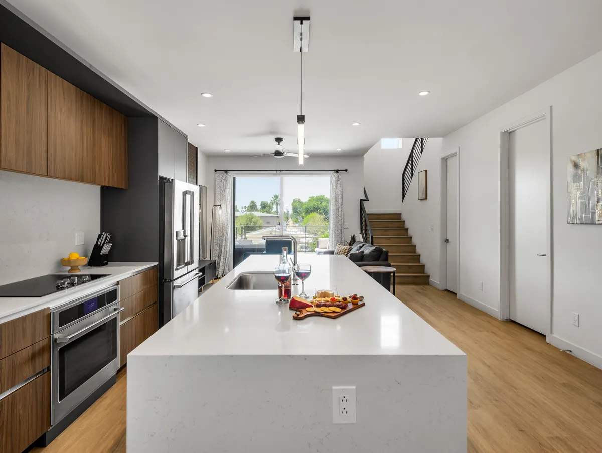A bright, cheerful kitchen space featuring a large island with bar seating, gleaming stainless steel appliances, and a substantial window that lets in plenty of natural light. The kitchen is arranged for both culinary activity and social interaction, with ample counter space and a welcoming atmosphere.